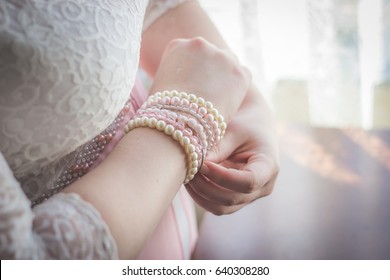 Woman putting on white and pink pearl beaded bracelets with focus on hands and wrist closeup in pink and white lace wedding dress as bridal preparation getting ready photos
