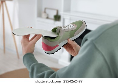 Woman putting orthopedic insole into shoe at home, closeup. Foot care