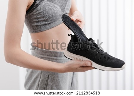 Woman putting orthopedic insole into shoe at home. Sports girl fitting orthopedic insole indoors, close up. Foot care banner. Flat Feet Correction. Treatment and prevention of foot diseases.