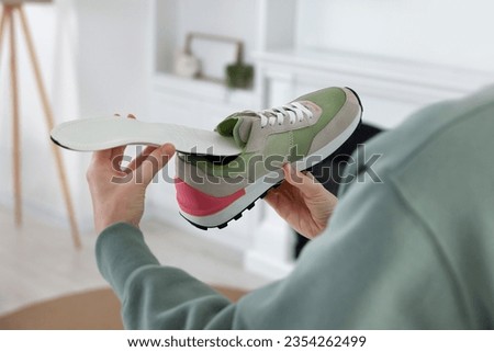 Woman putting orthopedic insole into shoe at home, closeup. Foot care