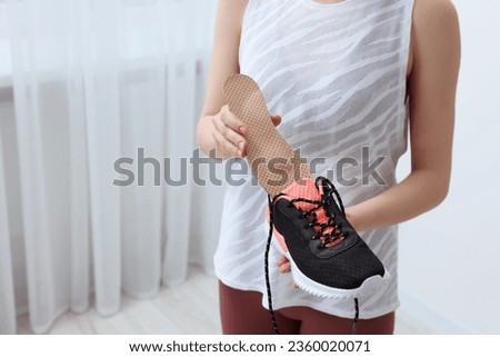 Woman putting orthopedic insole into shoe indoors, closeup and space for text. Foot care