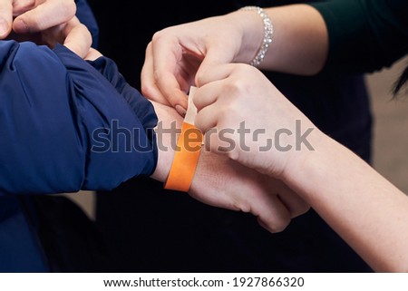 Woman putting a paper bracelet ticket on mans hand.