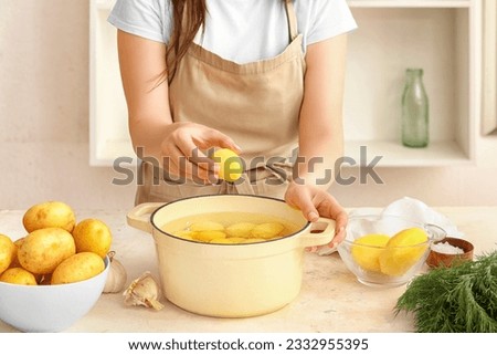 Woman putting peeled potato in pot at table in kitchen