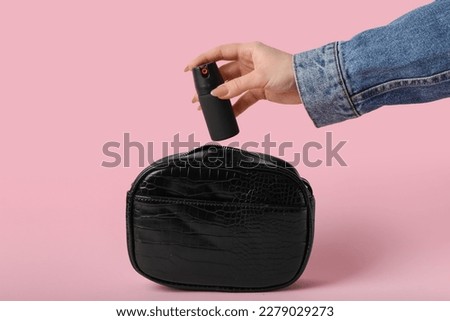 Woman putting pepper spray in bag on pink background