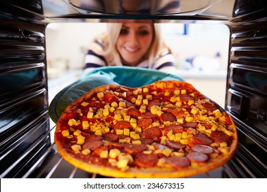 Woman Putting Pepperoni Pizza Into Oven To Cook