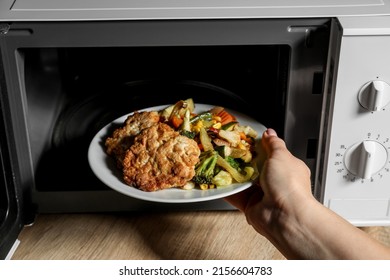 Woman Putting Plate With Delicious Food Into Microwave Oven On Wooden Table