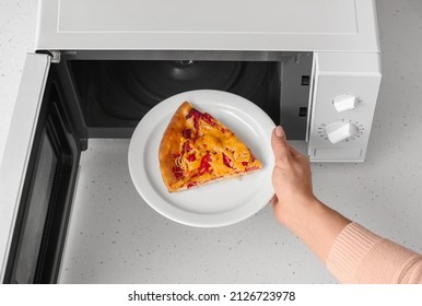 Woman Putting Plate With Piece Of Pizza Into Microwave Oven On Table, Closeup