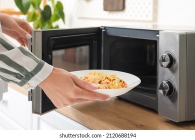 Mujer poniendo el plato de arroz con verduras en el horno microondas en la cocina