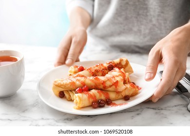 Woman Putting Plate With Thin Pancakes, Berries And Syrup On Table