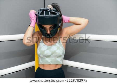 Woman putting protective headgear for practicing kickboxing standing in corner of ring boxing
