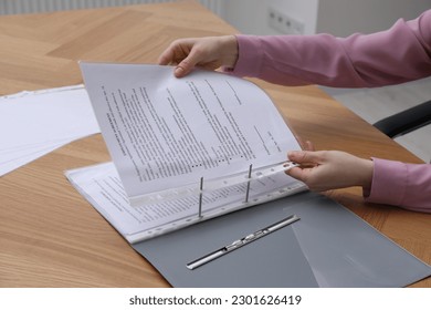 Woman putting punched pocket with document into folder at wooden table, closeup - Shutterstock ID 2301626419