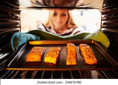 Woman Putting Salmon Fillets Into Oven To Cook