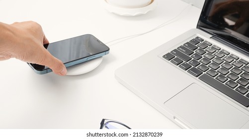 Woman Putting Smartphone Charging Power Battery With Wireless Charger Device Near Laptop Computer, Modern Technology Transfer Energy Mobile Phone On Workspace Desktop At Home Office