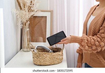 Woman putting smartphone into wicker basket with gadgets at home. Digital detox concept