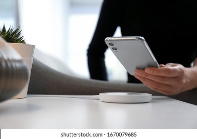 Woman putting smartphone on wireless charger in room, closeup. Space for text
