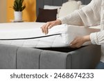 Woman putting soft orthopedic mattress on bed at home, closeup