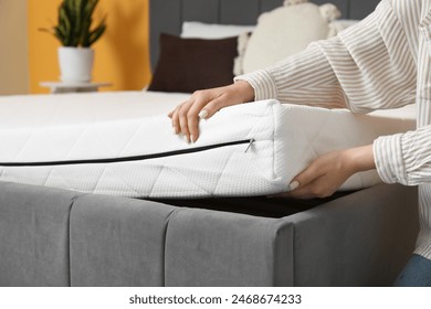 Woman putting soft orthopedic mattress on bed at home, closeup