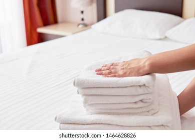 Woman putting stack of fresh white bath clean towels on bed sheet, copy space. Close up hands of hotel maid with towels. Room service - Shutterstock ID 1464628826