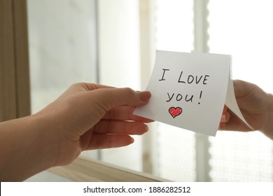Woman putting sticky note with text I love you! on mirror, closeup