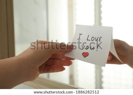Woman putting sticky note with text I love you! on mirror, closeup