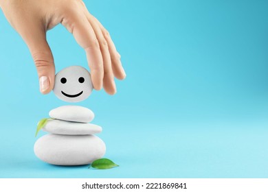 Woman putting stone with drawn happy face on stack against light blue background, closeup and space for text. Zen concept - Shutterstock ID 2221869841
