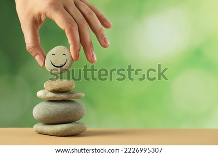 Woman putting stone with drawn happy face onto stack against blurred background, closeup and space for text. Zen concept