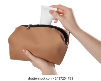 Woman putting tube of makeup product into cosmetic bag on white background, closeup