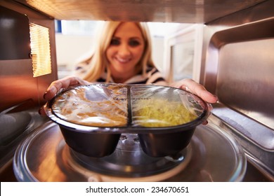 Woman Putting TV Dinner Into Microwave Oven To Cook