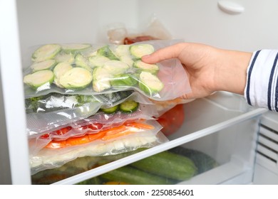 Woman putting vacuum bags with vegetables into fridge, closeup. Food storage