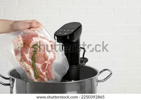 Woman putting vacuum packed meat into pot with sous vide cooker, closeup and space for text. Thermal immersion circulator
