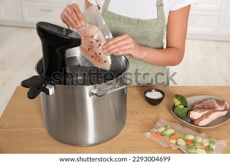 Woman putting vacuum packed meat into pot with sous vide cooker indoors, closeup. Thermal immersion circulator