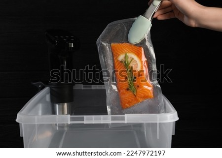 Woman putting vacuum packed salmon into box with thermal immersion circulator, closeup. Sous vide cooking