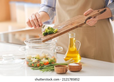 Woman putting vegetables in cooking pot on table in kitchen