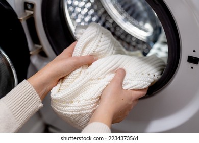 Woman putting white clothes into the drum of a washing machine, front view. Washing dirty clothes in the washer - Shutterstock ID 2234373561