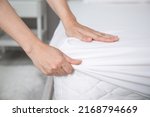 Woman putting white fitted sheet over mattress on bed indoors, closeup