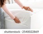 Woman putting white fitted sheet over new mattress on bed, closeup shot. Household chores concept