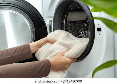 Woman putting white wool sweater into the drum of a washing machine in laundry room. Washing dirty clothes in the washer - Powered by Shutterstock