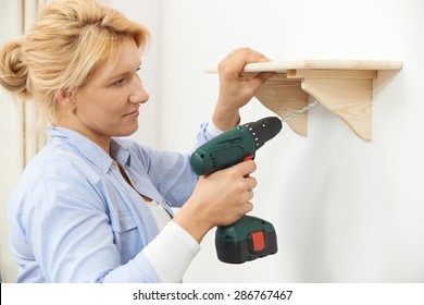 Woman Putting Up Wooden Shelf At Home Using Cordless Drill