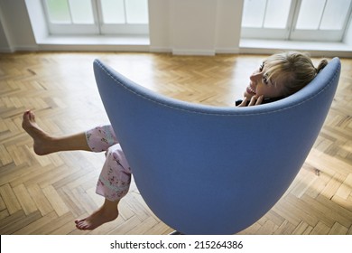 Woman In Pyjamas Sitting In Blue Armchair At Home, Using Cordless Phone, Smiling, Profile, Rear View