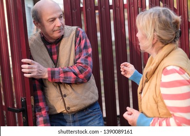 Woman Is Quarreling And Having Conflict With Her Neighbour At Fence Door. Man Is Afraid Of Her.