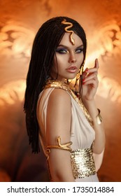 woman queen Cleopatra art photo. Creative golden makeup Black hair braids. Carnival ethnic egypt costume dress. Accessories jewelry snake bracelet, crown. Fashion model girl beautiful face close-up