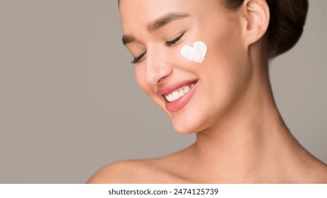 A woman with a radiant smile is shown with a white cream applied on her face. She appears content and relaxed as she enjoys a skincare routine. The cream visibly hydrates and nourishes her skin. - Powered by Shutterstock