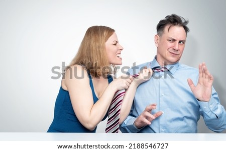 The woman in a rage grabbed the man by the tie and screams at him, the man covers himself with his hands and looks scared