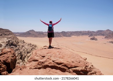 Woman with raised arms stands at viewpoint in Wadi Rum desert - valley Wadi Saabit. Jordan