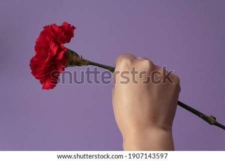 Woman with raised fist holding red carnation against purple background. Freedom, Revolution and April 25 concept