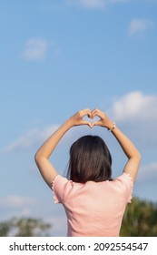 A woman raises her hand above her head to make a heart symbol on the background of the bright morning sky because the heart symbol signifies love, friendship and kindness to one another.
