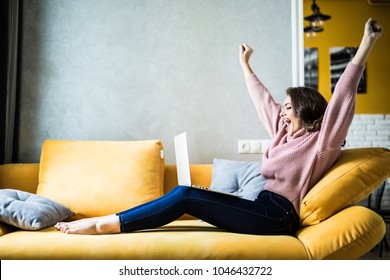 Woman Raising Her Hands Up On The Couch With Laptop At Home