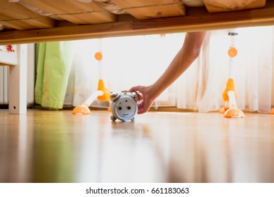 Woman Reaching Under The Bed And Pressing Snooze Button On Alarm Clock