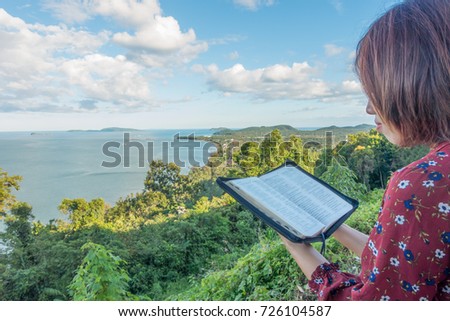 Woman reading bible on Mountain with sky and sea background