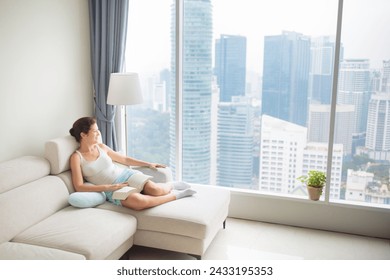 Woman reading a book at big window with city view. Young female enjoying calm quiet time with books. People read and relax. Modern apartment in high rise building. - Powered by Shutterstock